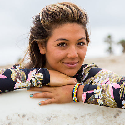 Surfer girl wearing Love Is Project Rainbow LOVE bracelet pride