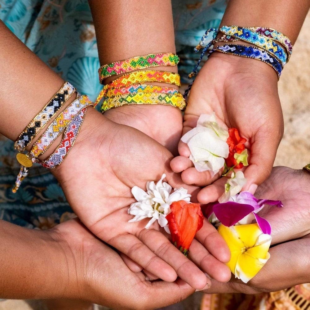 A group of models holding flowers and wearing the  Quartz Bali Friendship Bracelet Bundle from Love Is Project